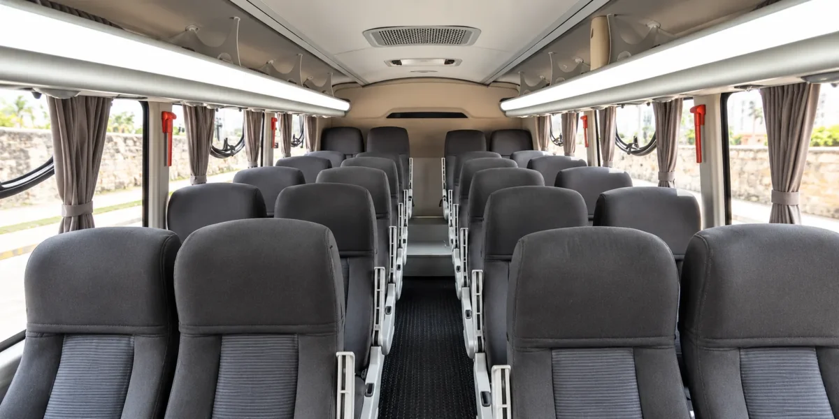 Fileiras de poltronas e ar-condicionado dentro do ônibus Coaster de traslados